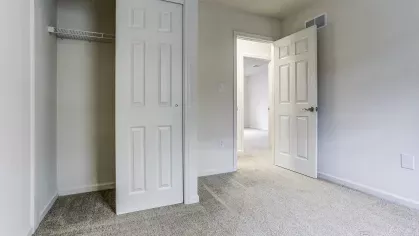 Interior view of a third bedroom with open sliding closet, plush carpet flooring, and neutral walls perfect for a flexible living space or home office.