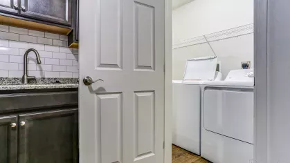 In-unit laundry area with full-size washer and dryer, white shelving, and wood-style flooring conveniently located off the kitchen.