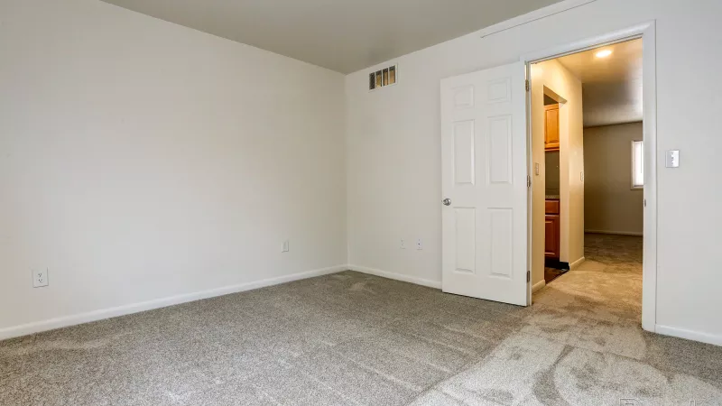 Empty bedroom at Rosedale apartments with light gray carpet and an open door leading to an adjacent room, ready for personalization.