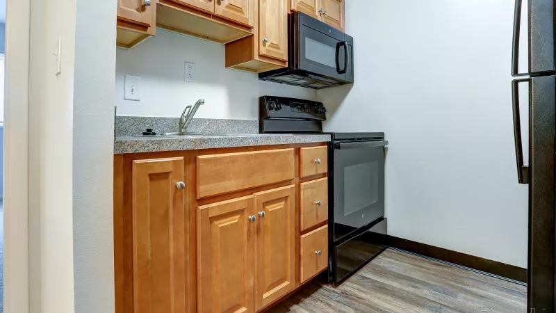 Compact kitchen at Rosedale with wooden cabinetry, a dark countertop, stainless steel sink, black microwave, and black electric stove.