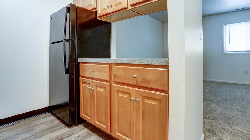 View of the kitchen at Rosedale, showing a black refrigerator, wooden base cabinets with dark countertops, and open concept to the living area.