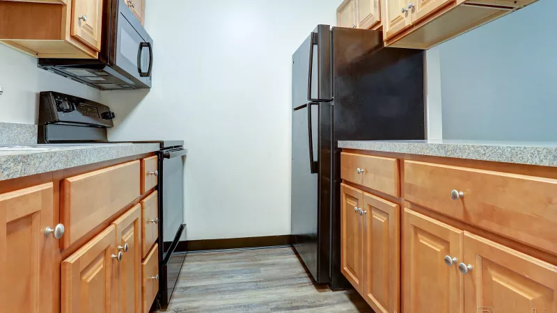 Well-appointed kitchen at Rosedale with light wood cabinets, dark countertops, black refrigerator, stove, and microwave, featuring wood-style flooring.