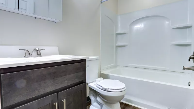 Modern renovated bathroom at Rosedale featuring a dark wood vanity with a white countertop, toilet, and a white shower-bathtub combination.