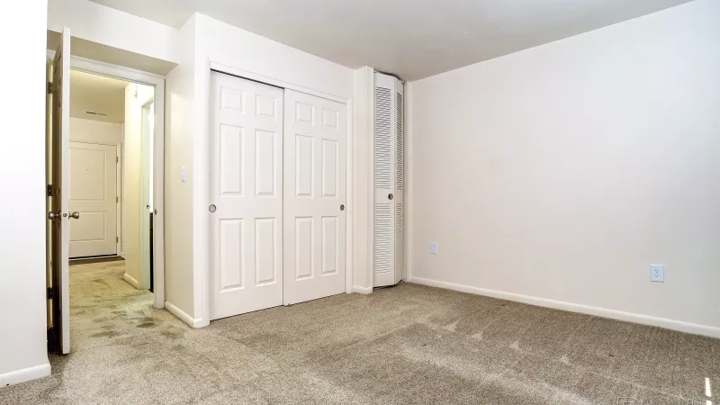 Renovated bedroom at Rosedale with light carpet, white sliding closet doors, and a doorway leading to the entry or hallway.