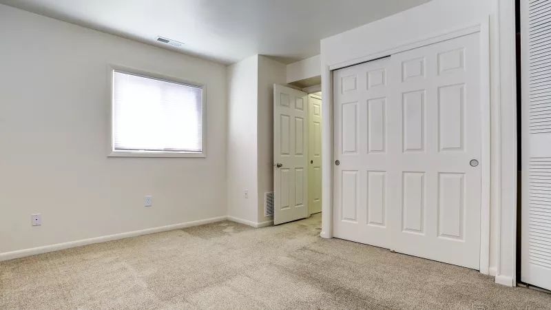 Renovated bedroom at Rosedale with light carpet, a large window, and white bi-fold closet doors, offering ample storage space.