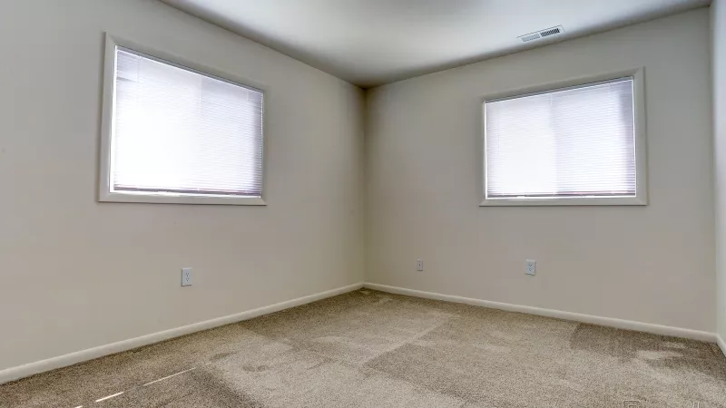 Spacious, bright bedroom in a renovated Rosedale apartment with two large windows and plush carpet, ready for furnishings.