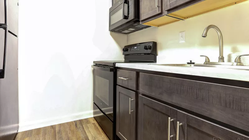 Modern renovated kitchen at Rosedale with dark cabinetry, white countertops, black appliances including a stove, microwave, and stainless steel sink.