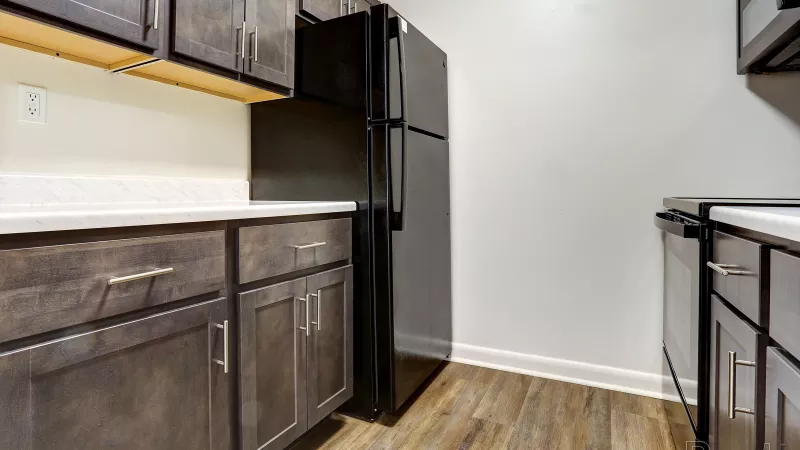 Modern renovated kitchen at Rosedale with dark wood cabinets, white countertops, and a large black refrigerator, offering contemporary style.