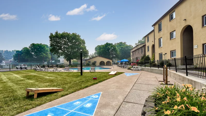 Vibrant outdoor amenities at Rosedale apartments, including a sunny lawn with cornhole, a shuffleboard court, and the community pool area with lounge chairs.