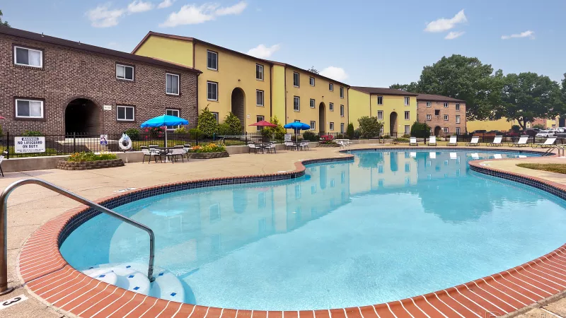 Expansive view of the Rosedale apartment complex and its inviting swimming pool with ample seating and umbrellas, showcasing the community's outdoor lifestyle.