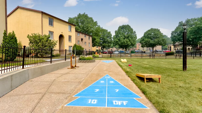 Outdoor shuffleboard court at Rosedale apartments, ready for resident recreation, with apartment buildings and trees in the background.