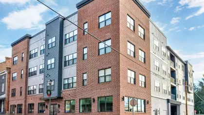 The modern exterior of the Riverview Terrace apartment building, showcasing a stylish blend of traditional brick and contemporary gray siding with large windows, indicating a vibrant downtown living experience.