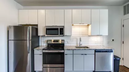 Contemporary kitchen at Stadium Row featuring white cabinetry, stainless steel appliances including a refrigerator and dishwasher, and granite countertops.
