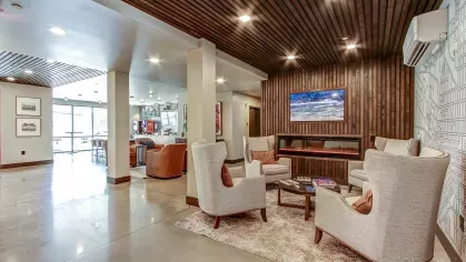 Luxurious clubhouse lounge at Stadium Row with stylish seating, a modern fireplace, wood slat ceiling, and a view into the cafe area.