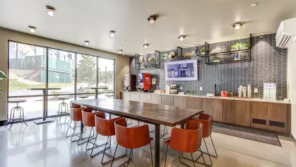 Bright clubhouse cafe at Stadium Row with a long communal table, comfortable seating, large windows, and a fully equipped coffee bar for residents.
