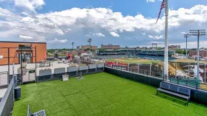 Rooftop dog park at Stadium Row overlooking a baseball stadium, featuring artificial turf, seating areas, and an American flag, ideal for pets and their owners.
