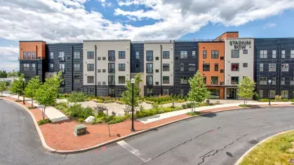 Striking exterior of Stadium Row apartment building with modern architecture, a mix of dark and orange siding, and ample landscaping, showcasing the vibrant community.