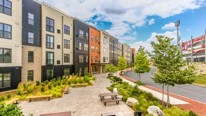 Outdoor communal space at Stadium Row featuring modern apartment buildings, lush landscaping, picnic tables, and grilling stations, perfect for residents to relax and socialize.