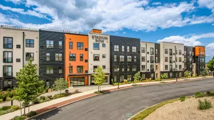 Modern apartment complex at Stadium Row with varied facade colors including black, grey, and orange, showcasing contemporary architecture and the 'Stadium Row' sign, under a blue sky with clouds.