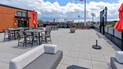 Vibrant rooftop patio at Stadium Row with lounge seating, picnic tables, red umbrellas, string lights, and a view of the baseball stadium, perfect for enjoying Harrisburg.