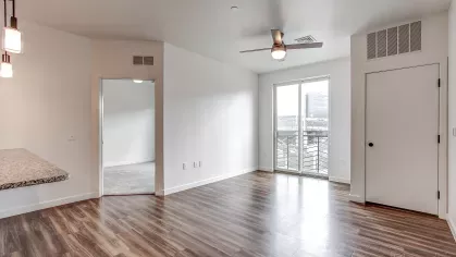 Living area in the Slugger 208 floor plan at Stadium Row, featuring wood-style flooring, a ceiling fan, and sliding glass doors leading to a private balcony.