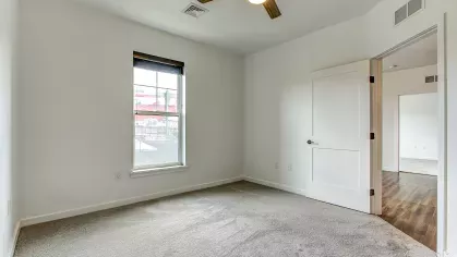 Bedroom in the Slugger 208 floor plan at Stadium Row, featuring soft gray carpet, a ceiling fan, and a large window providing natural light.