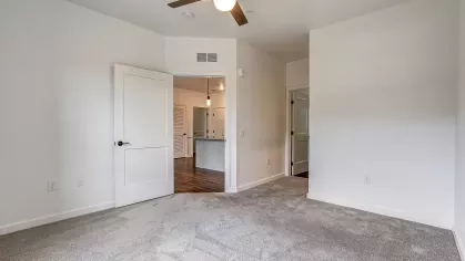 Bedroom in the Slugger 208 floor plan at Stadium Row, featuring a ceiling fan, comfortable carpet, and open doorways leading to a closet and the main living space.