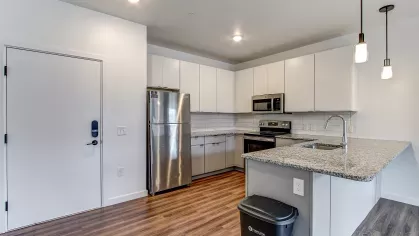 Spacious entry and kitchen area in the Slugger 208 floor plan at Stadium Row, featuring white cabinets, stainless steel appliances, a large island, and wood-style flooring.