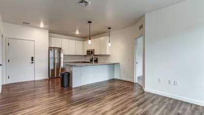 Spacious kitchen in the Slugger 208 floor plan at Stadium Row with white cabinetry, stainless steel appliances, granite countertops, and an island with pendant lighting, opening to the living area.