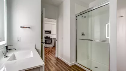 Modern bathroom in the Stretch 423 floor plan at Stadium Row, featuring a sleek white vanity with a large mirror, toilet, and a combined shower and bathtub.