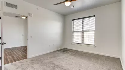 Comfortable bedroom in the Stretch 423 floor plan at Stadium Row, with soft gray carpet, neutral walls, and a large window providing bright natural light.