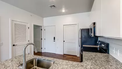Contemporary kitchen in the Stretch 423 floor plan at Stadium Row, featuring dark wood cabinets, light granite countertops, stainless steel appliances, and a kitchen island with a sink.