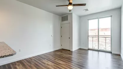 Open-concept living room in the Stretch 423 floor plan at Stadium Row, highlighting wood-style flooring, a large window, and seamless flow into the modern kitchen area.