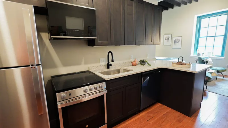 Modern L-shaped kitchen with granite countertops, dark cabinetry, and stainless steel appliances at Prince Street Lofts