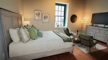 Spacious studio apartment with large windows, a queen bed, seating area, and mounted TV at Prince Street Lofts