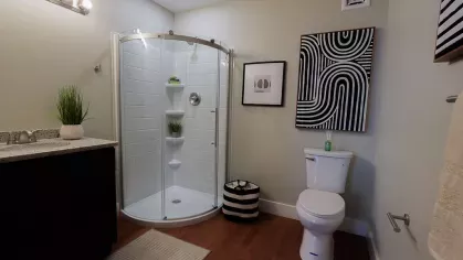 Modern bathroom with glass shower, vanity lighting, and decorative wall art at Prince Street Lofts