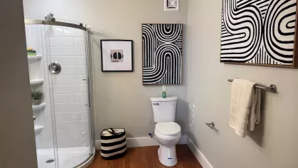 Spacious bathroom with glass shower, modern vanity, and black-and-white abstract wall art at Prince Street Lofts