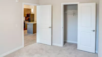 Inside a bedroom at Riverview Terrace, featuring a convenient open closet with ample hanging space and a doorway leading into the spacious open concept kitchen and living area, highlighting apartment flow