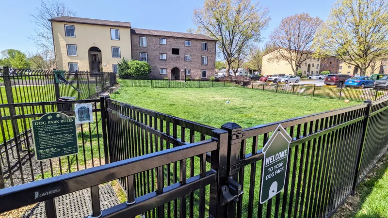 Fenced dog park at Rosedale apartments, providing a spacious grassy area for pets to play, with clear rules posted.