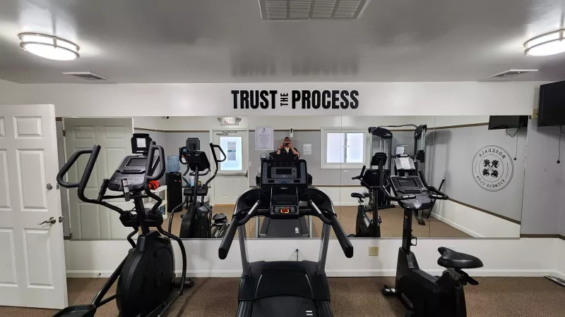 Comprehensive fitness center at Rosedale featuring a variety of cardio equipment, including treadmills and ellipticals, with large mirrors and a motivational "TRUST THE PROCESS" sign.