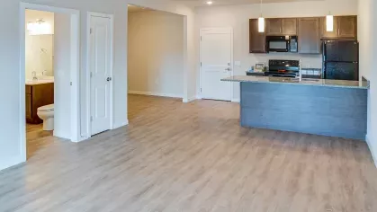 The welcoming entryway of an apartment at Riverview Terrace, showcasing the seamless transition to the open concept kitchen with an island and modern appliances, and a convenient adjoining bathroom to the left.