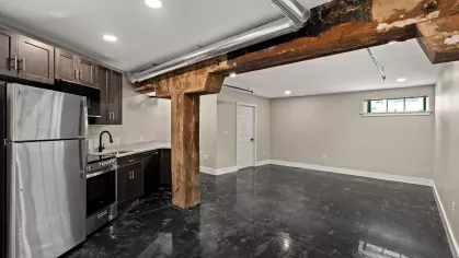 Open-concept kitchen and living area at Prince Street Lofts, featuring exposed wood beams, polished concrete floors, and stainless steel appliances.