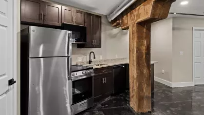 Modern kitchen with dark wood cabinets, granite countertops, stainless steel appliances, and overhead ductwork for an industrial loft feel.