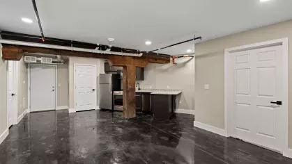 Spacious studio layout with exposed beams and black concrete floors, showcasing modern finishes and natural light from overhead fixtures.