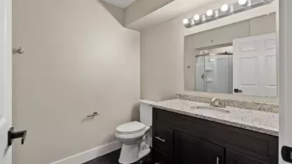 Contemporary bathroom with granite vanity, dark cabinetry, large mirror, and a walk-in shower with white tile surround.