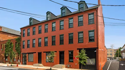 Front exterior view of Prince Street Lofts, highlighting its classic red-brick design with black-trim windows and three entrances along the sidewalk.