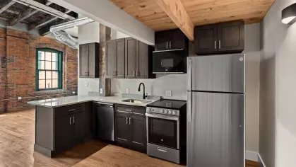 Contemporary kitchen with granite countertops and dark cabinetry, set against industrial details like exposed ducts and rustic brick walls.