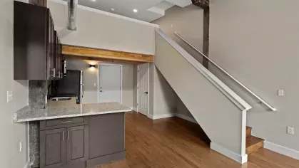 Entryway and kitchen view with exposed ceiling beams, granite breakfast bar, and staircase leading to lofted space.