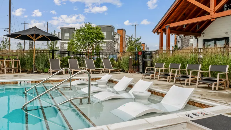 Resort-style outdoor swimming pool at The Foundry with in-water lounge chairs, shaded seating, and modern landscaping in a secure fenced area.
