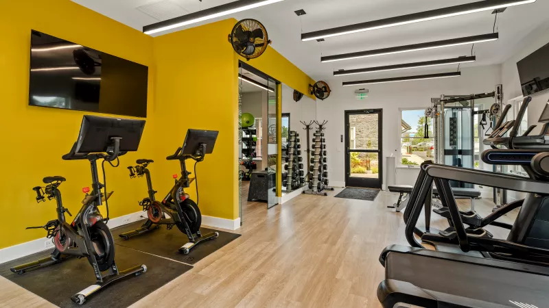 State-of-the-art fitness center at The Foundry featuring Peloton bikes, treadmills, weight racks, and a vibrant yellow accent wall.